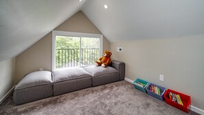 Un dormitorio acogedor en el ático con un ventanal grande, un sofá mullido y un osito de peluche.