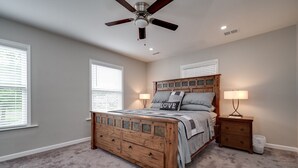 Un dormitorio con una cama de madera, dos mesitas de noche, un ventilador de techo y una ventana con persianas.
