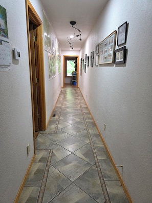 A hallway with patterned floor tiles, framed pictures on the walls, and a door on the left.