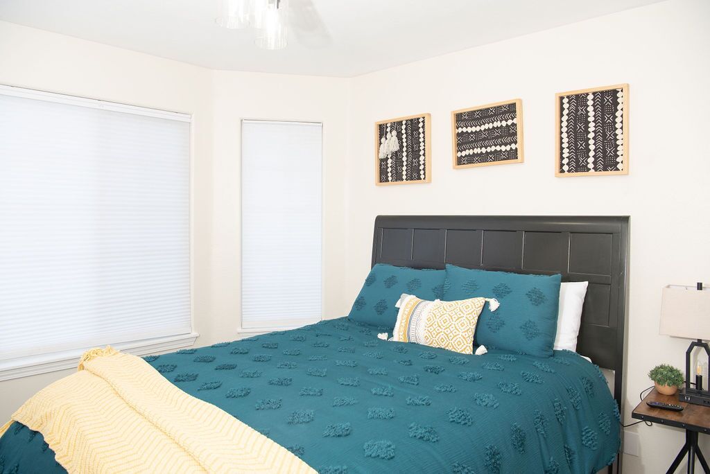 A bedroom with a dark headboard, teal bedding, and three framed wall art pieces.