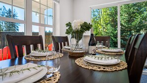 A dining table set for four with woven placemats, white plates, and a bottle of wine. - Peaceful Parkside Cottage (Courtenay)