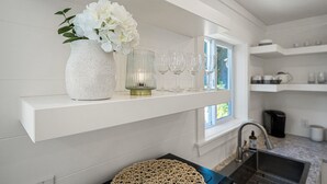 A kitchen with white cabinetry, a white vase with flowers, and wine glasses on a shelf. - Peaceful Parkside Cottage (Courtenay)