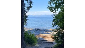 A coastal path leading to a beach with a view of the ocean and distant mountains. - Peaceful Parkside Cottage (Courtenay)