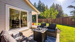 A patio area with a sliding glass door, a table, and outdoor furniture. - Peaceful Parkside Cottage (Courtenay)