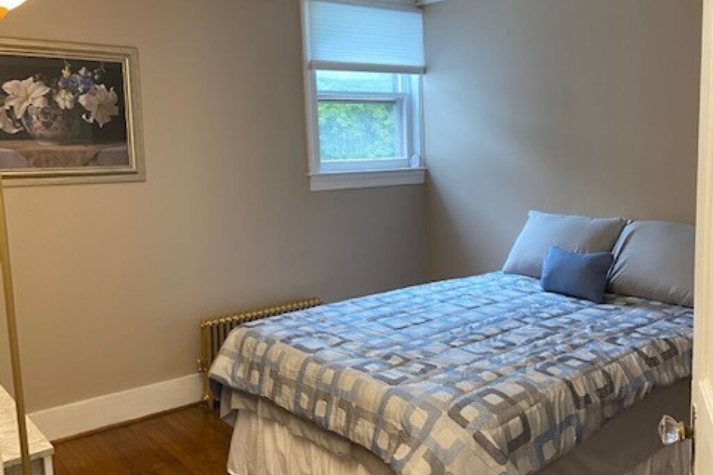Une chambre à coucher avec un lit, un radiateur, une fenêtre et un tableau accroché au mur.