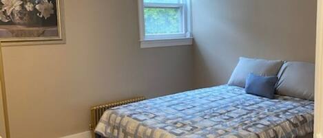 Une chambre à coucher avec un lit, un radiateur, une fenêtre et un tableau accroché au mur.