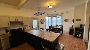 A kitchen with a central island, white cabinets, a stove, and a dishwasher. There is a dining area with a table and chairs. - Downtown Dream in Owensboro Ky (Owensboro)