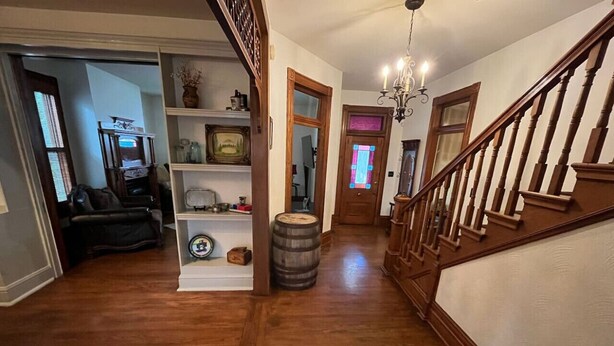 A wooden-floored hallway with a staircase, a bookshelf, and a door with a stained glass window. - Downtown Dream in Owensboro Ky (Owensboro)