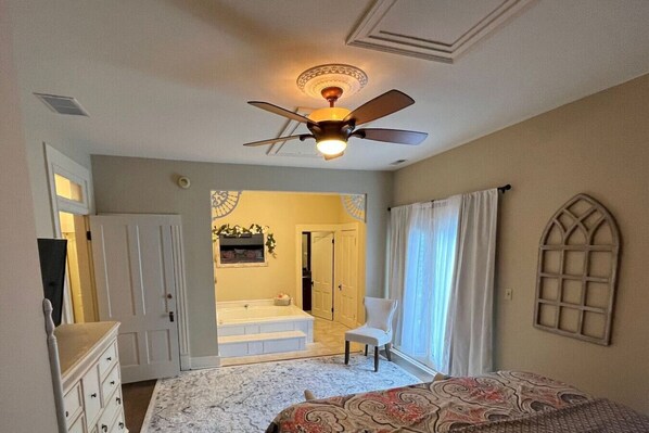 Un dormitorio con cama, una silla, ventilador de techo y ventana con cortinas.