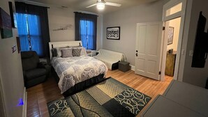 A bedroom with a bed, a chair, a desk, a ceiling fan, and a door. - Downtown Dream in Owensboro Ky (Owensboro)