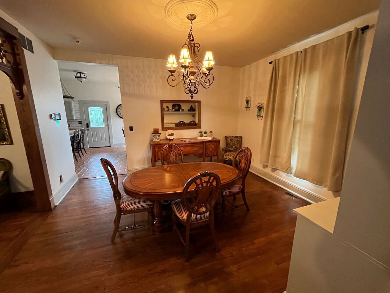 Un comedor con una mesa y sillas de madera, una araña y una ventana con cortinas.