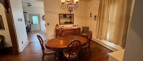 Un comedor con una mesa y sillas de madera, una araña y una ventana con cortinas.