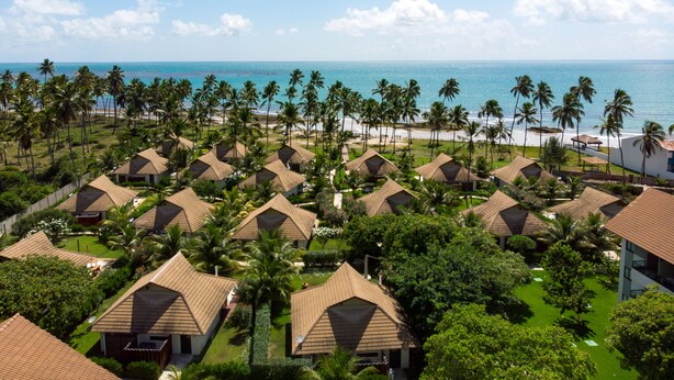 Ein Resort mit mehreren bungalowsartigen Gebäuden, einem Strand und Palmen.