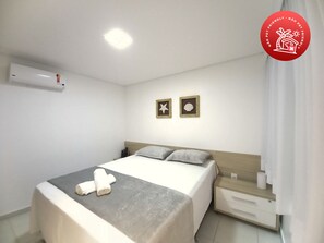 Ein Hotelzimmer mit einem Bett, einem Nachttisch, einer wandmontierten Klimaanlage und zwei gerahmten Bildern.