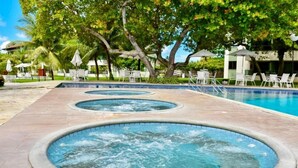 Ein Poolbereich mit drei Whirlpools, umgeben von Liegestühlen und Sonnenschirmen.