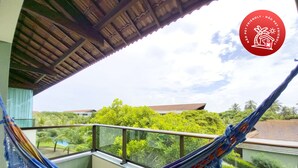 Eine Hängematte auf einem Balkon mit Blick auf üppiges Grün und Gebäude im Hintergrund.