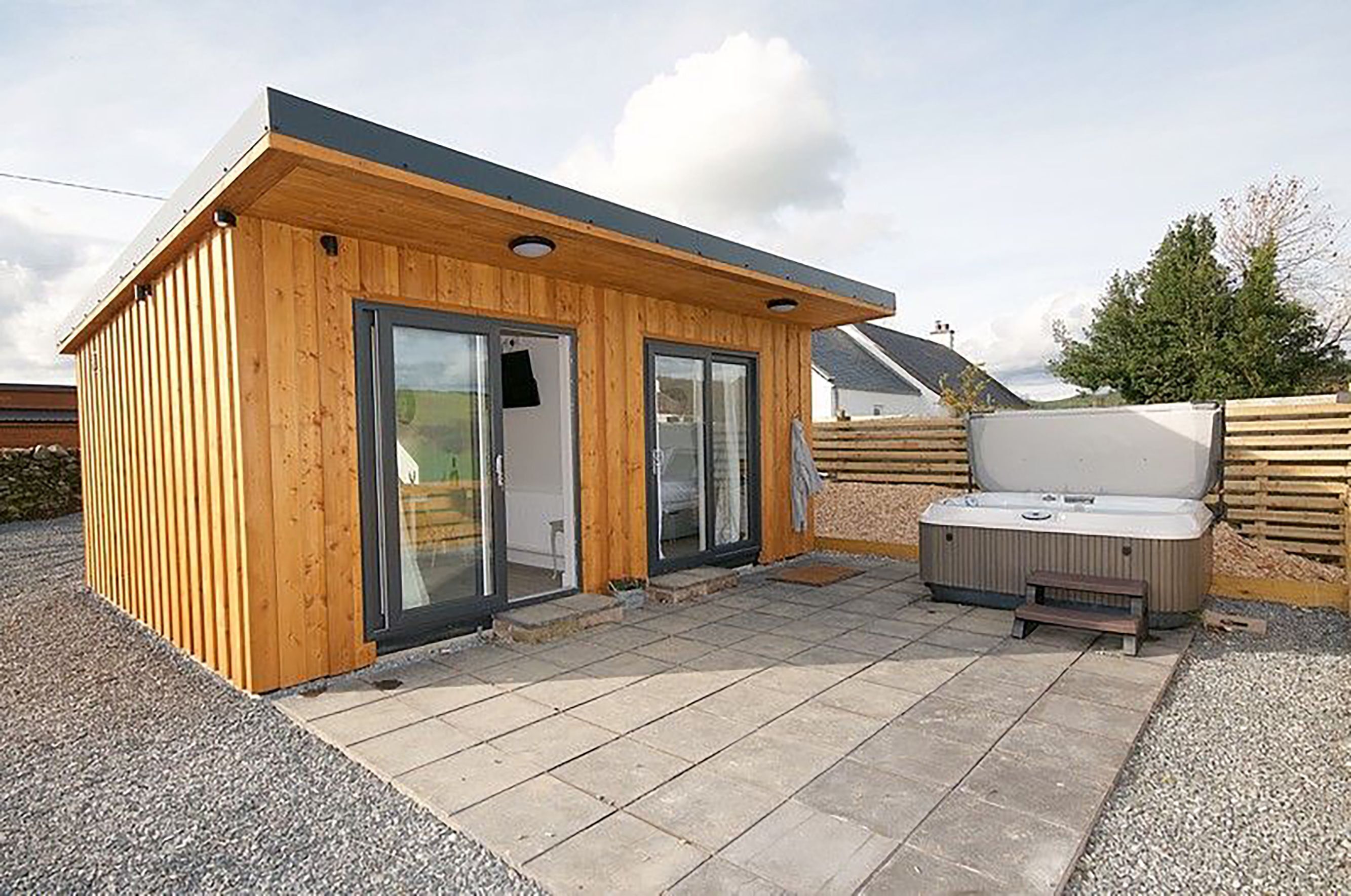 Une petite cabane en bois dotée d’un patio comprenant un banc et un jacuzzi.