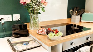 A kitchen counter with a vase of flowers, a bowl of fruit, a plate of pastries, and a digital device. - Beths Bothy -  a pod that sleeps 2 guests  in 1 bedroom (Gatehouse of Fleet)