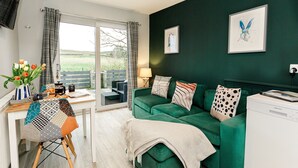 A modern living room with a green sofa, a coffee table, and a view of the outdoors through a glass door. - Beths Bothy -  a pod that sleeps 2 guests  in 1 bedroom (Gatehouse of Fleet)