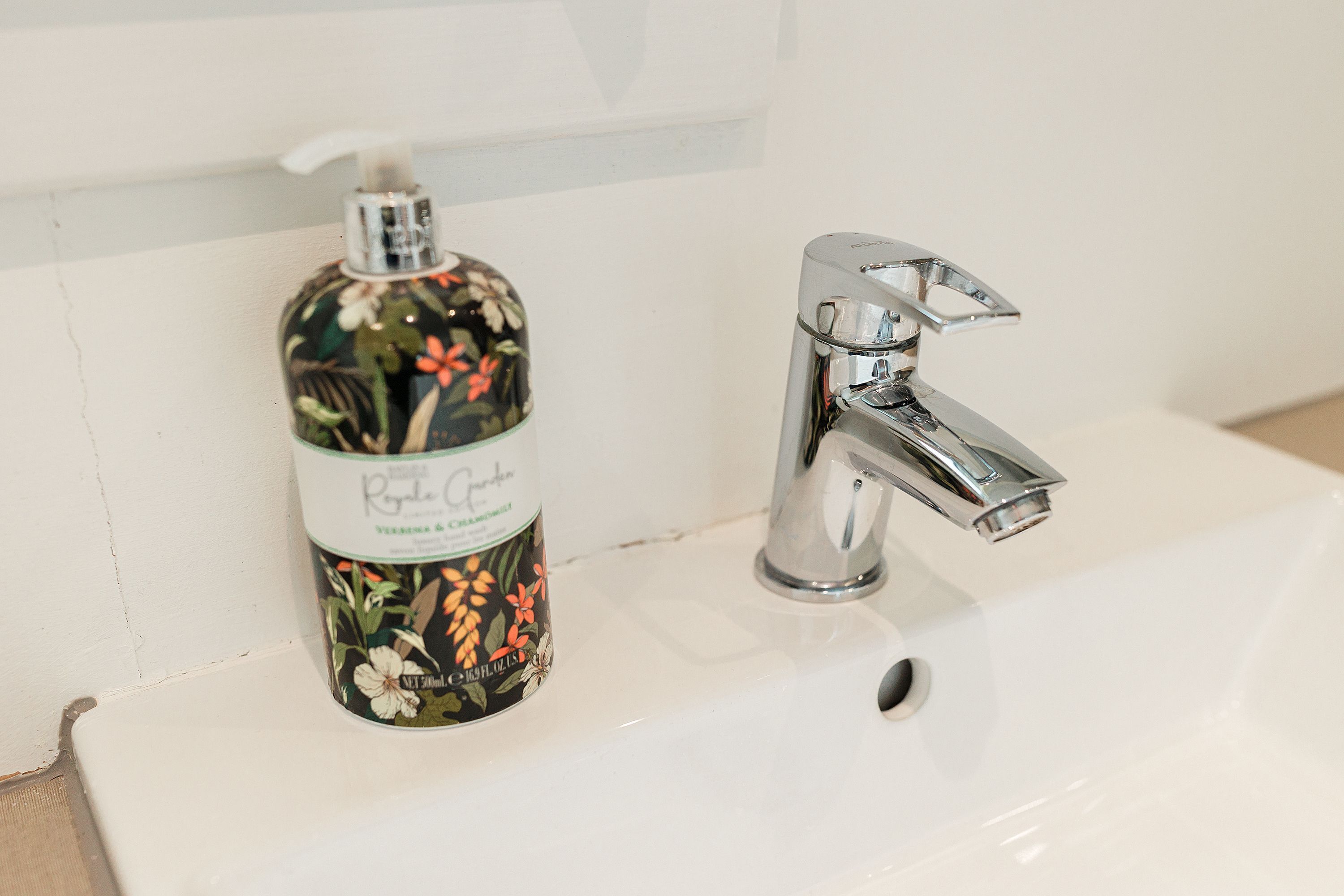 Een wastafel met een chromen kraan en een zeepdispenser met bloemenprint.