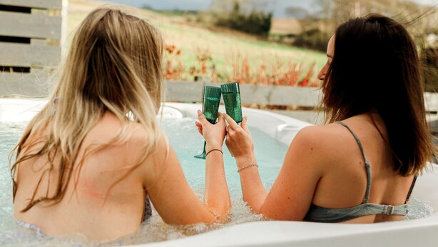 Two people in a hot tub, holding green glasses.