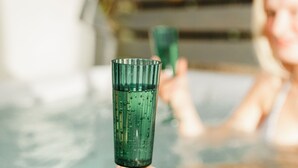 A person holding a green glass in a hot tub with a wooden deck in the background.