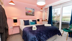 A bedroom with a large bed, a bedside table with a lamp, a mirror, and a view of the outdoors through a sliding door.