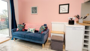 A cozy living room with a blue sofa, a small table, a white cabinet, and a dishwasher.