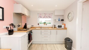 A compact kitchen with white cabinets, a microwave, a sink, and a window with a floral curtain.