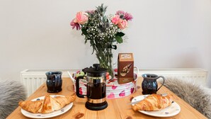 A breakfast table with croissants, a coffee pot, a box of butter shortbread, and a vase of flowers.