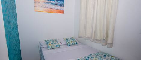 Habitación con cama individual, una pintura de atardecer en la playa, cortina y ropa de cama estampada.