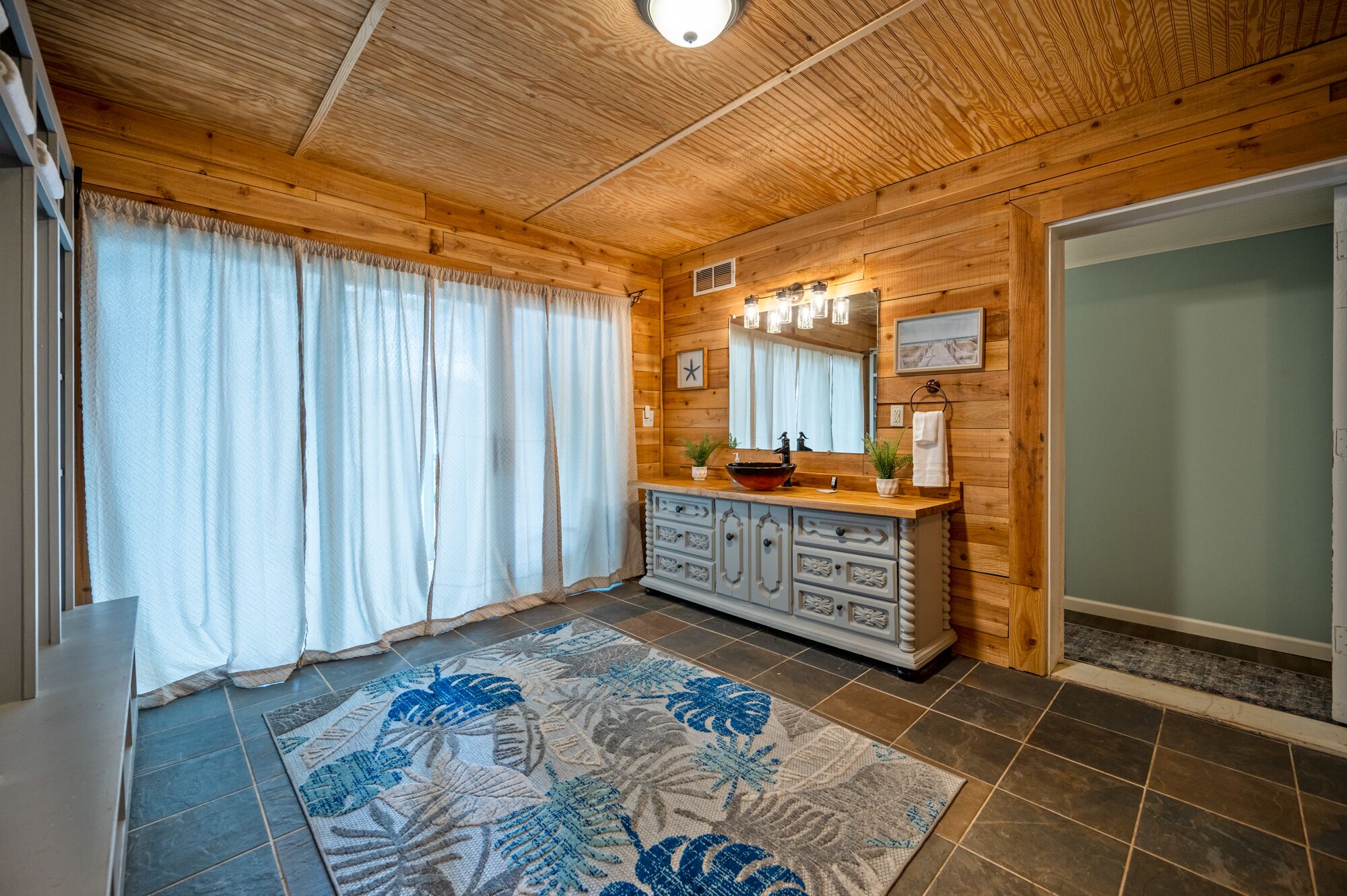 A wooden cabin interior with a bathroom featuring a vanity, mirror, and shower.
