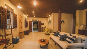 A spacious living room with a wooden ceiling, a white sofa with striped cushions, a wooden coffee table with fruit, and a wicker basket. - Vila Gameleira Garça Torta (Maceió)