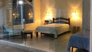 A bedroom with a glass partition, two beds, bedside lamps, and a small table. - Vila Gameleira Garça Torta (Maceió)
