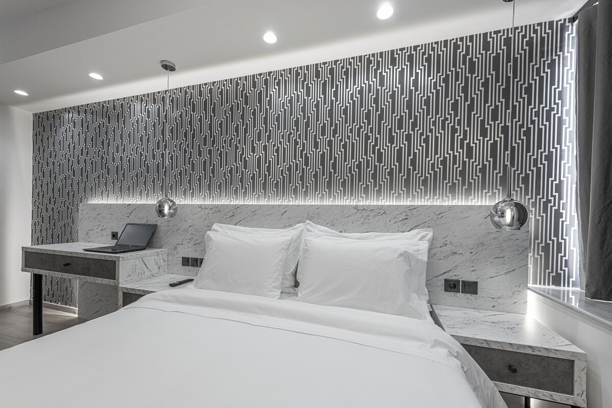 Ein modernes Schlafzimmer mit Marmorkopfstück, einem Nachttisch mit Laptop und einem großen Bett mit weißer Bettwäsche.