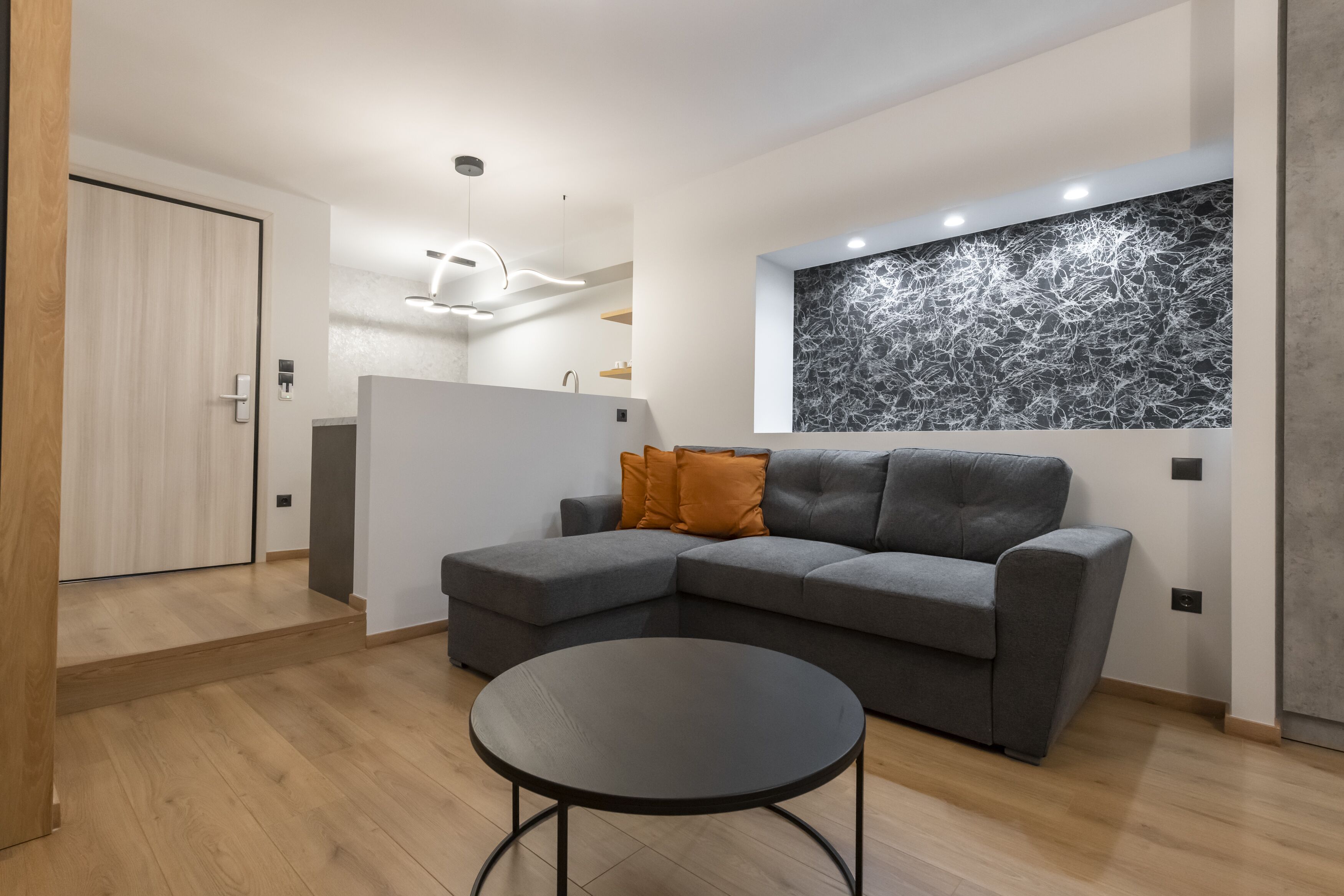 Een moderne woonkamer met een grijze hoekbank, een zwarte salontafel en een houten vloer.
