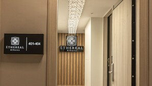 Un pasillo con piso de madera, un letrero que dice 'ETHEREAL Athens' con un número de teléfono y una puerta con picaporte de metal.