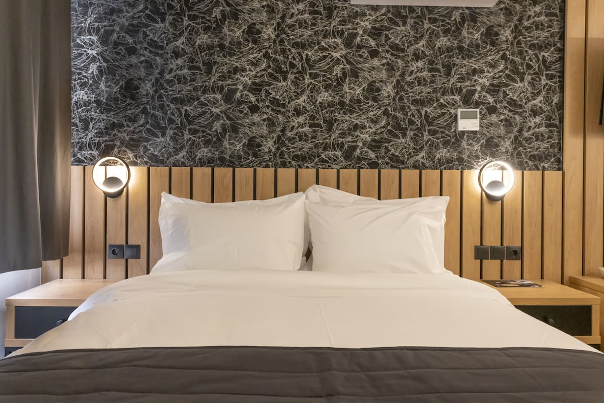 A hotel room with a bed, wooden headboard, two bedside tables, and a wall with a textured pattern.