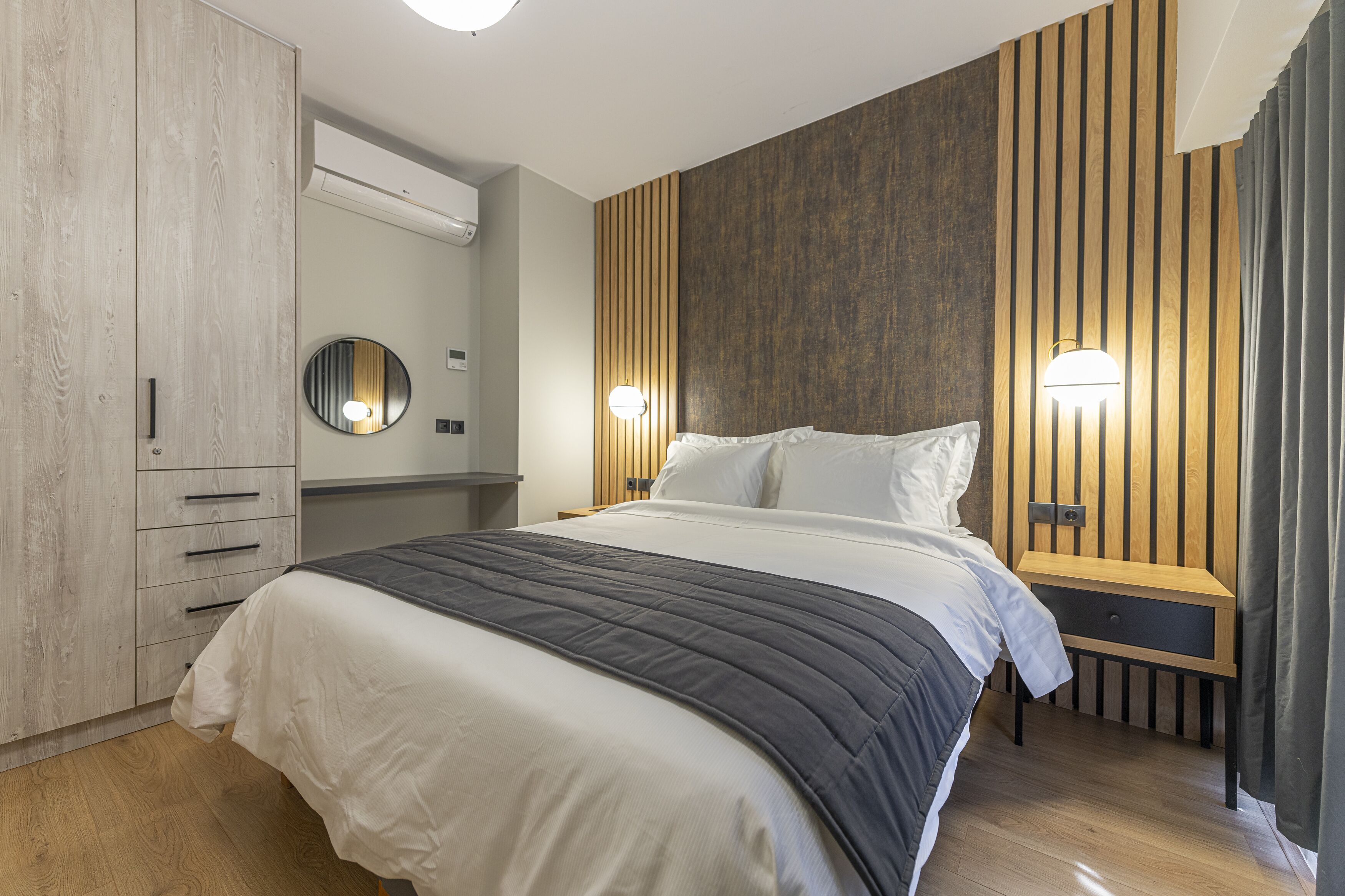 A modern bedroom with a large bed, wooden panel wall, bedside lamps, and a wardrobe.