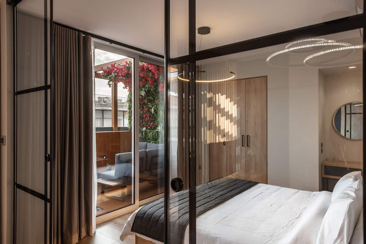 A modern bedroom with a large bed, a sliding glass door leading to a balcony, a wooden wardrobe, and a round mirror.