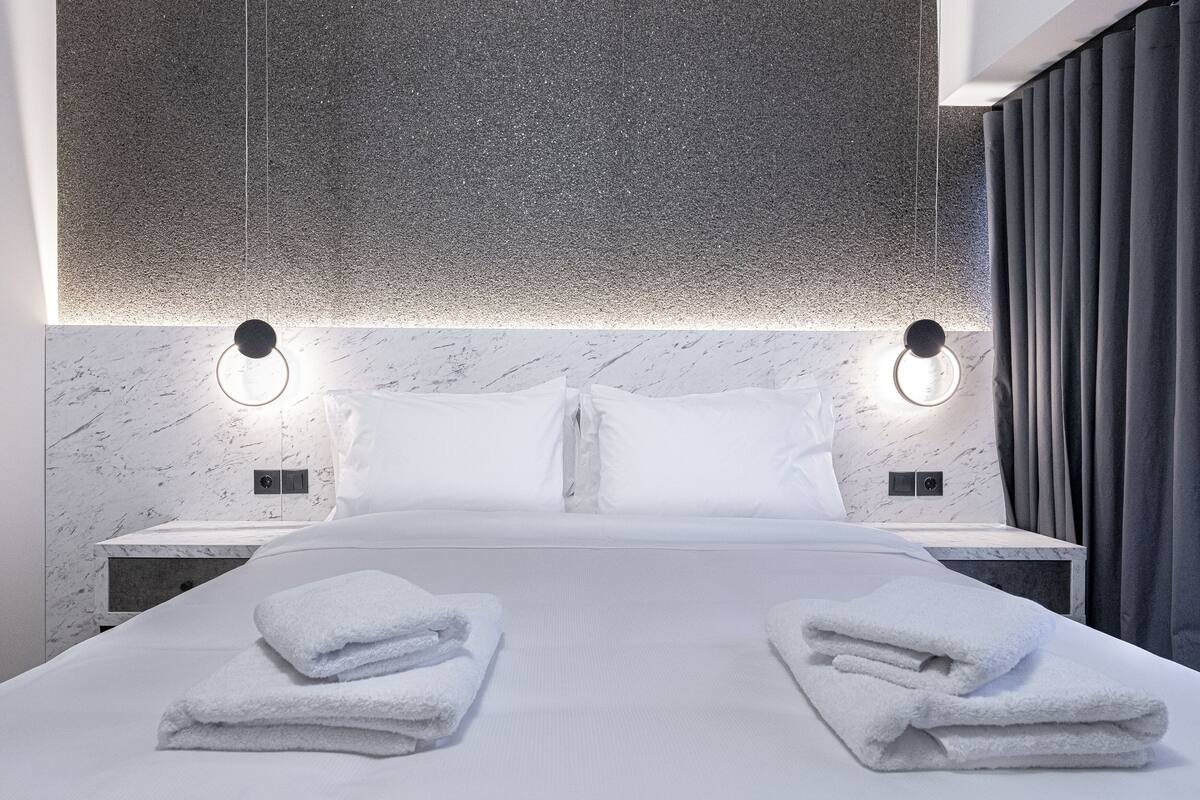 A modern hotel room with a large bed, two bedside tables, and a headboard with integrated lighting.