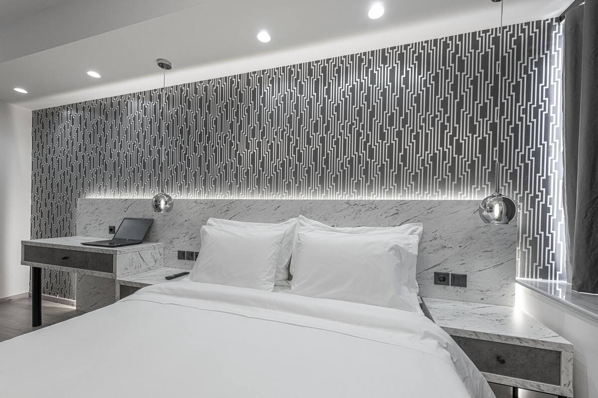 A modern bedroom with a marble headboard, a bedside table with a laptop, and a large bed with white bedding.