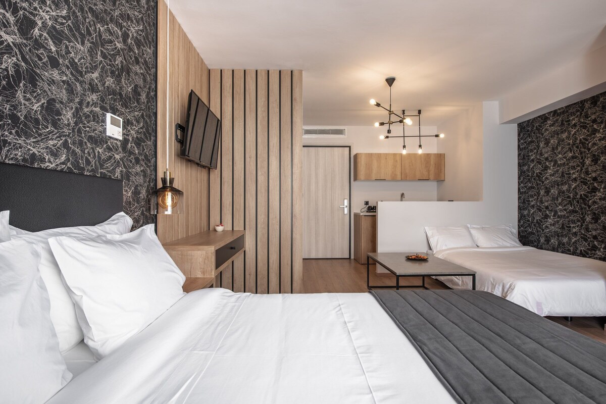 Ein modernes Hotelzimmer mit zwei Betten, einer Holzwand, einem Fernseher, einem Schreibtisch und einer kleinen Küchenzeile.
