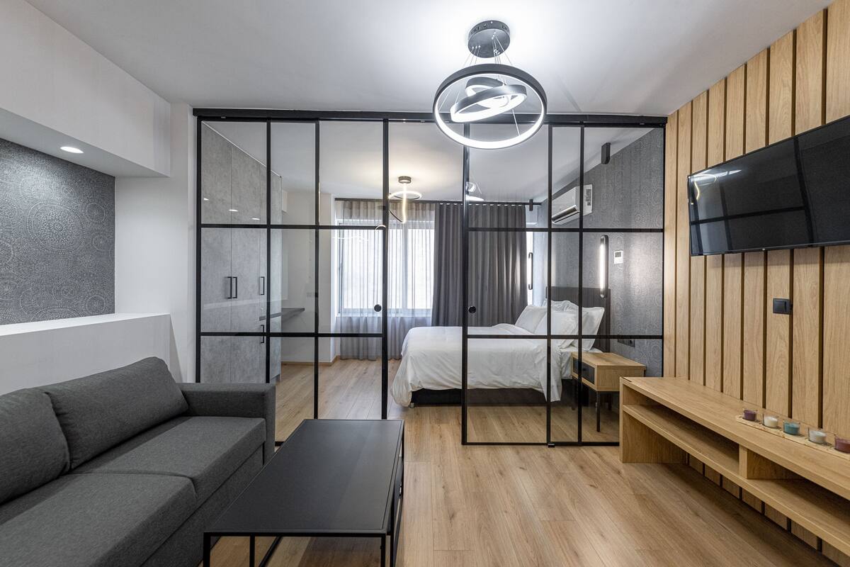 A modern hotel room with a bed, a sofa, a TV, and a wooden panel wall.