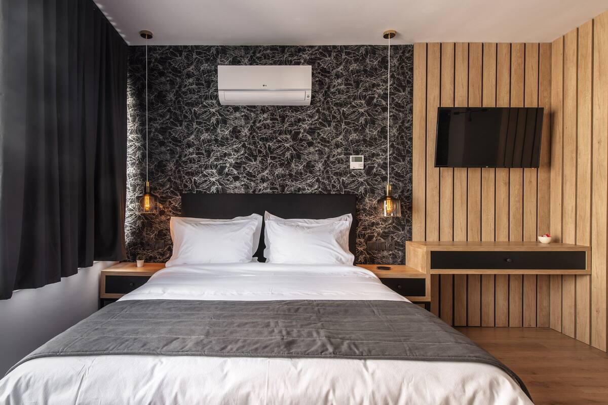 A modern bedroom with a large bed, a flat-screen TV, an air conditioner, and a unique textured wall.