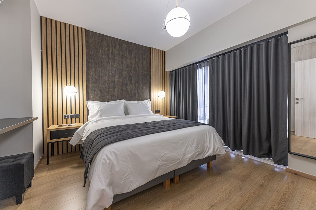 A modern bedroom with a large bed, wooden panel wall, two bedside tables, and a wardrobe.