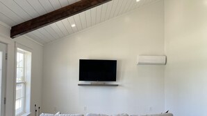 A spacious living room with a large grey sectional sofa, a mounted flat-screen TV, and a wooden ceiling beam.