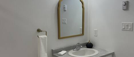 A bathroom with a white toilet, a sink with a gold-framed mirror above it, and a wall-mounted light fixture.