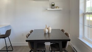 A dining area with a dark wooden table, four chairs, and two white floating shelves above it.