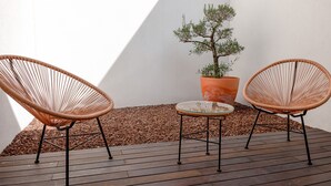 Two wicker chairs and a small table on a wooden deck with a potted plant.